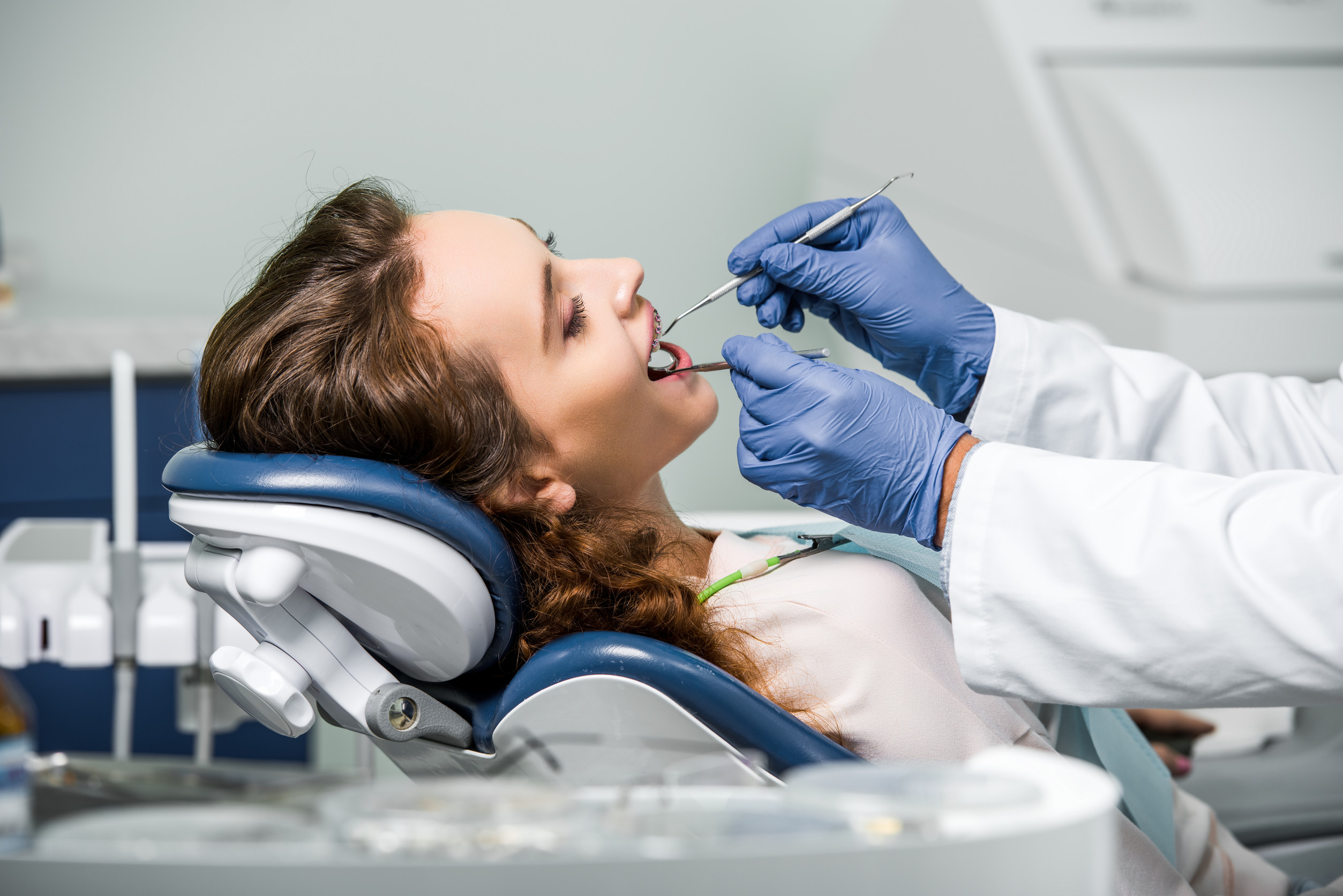 cropped view of dentist in latex gloves examining teeth of woman in dental clinic