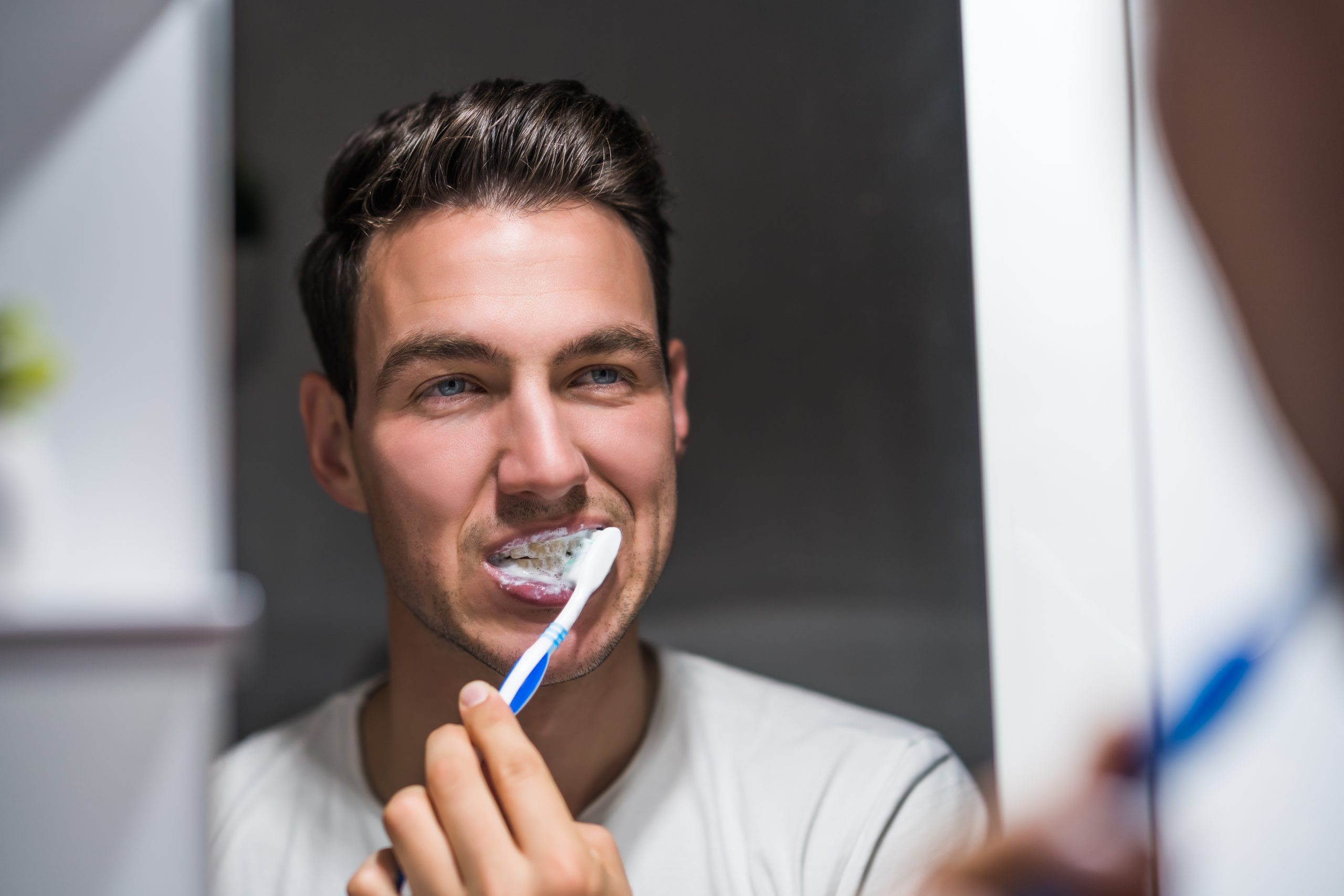 Man is brushing teeth while looking himself in the mirror.